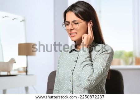Young woman in eyeglasses suffering from ear pain indoors Royalty-Free Stock Photo #2250872237