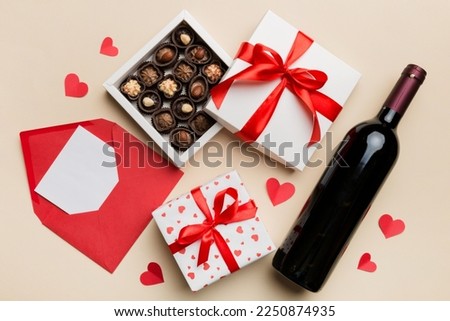 Bottle of red wine on colored background for Valentine Day with gift box, envelope and chocolate. Heart shaped with gift box of chocolates top view with copy space.