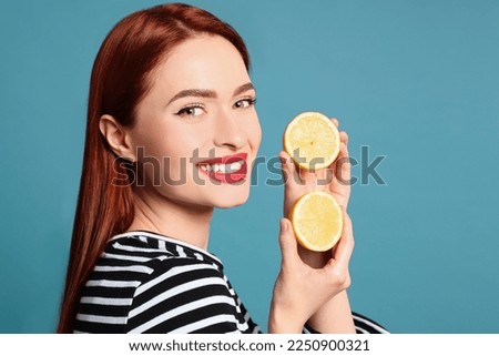 Happy woman with red dyed hair and lemons on light blue background