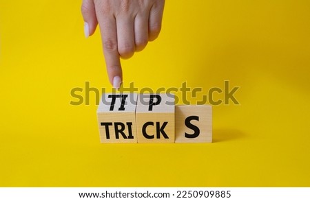 Tips and Tricks symbol. Businessman Hand points at wooden cubes with words Tricks and Tips. Beautiful yellow background. Business and Tips and Tricks concept. Copy space
