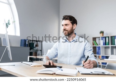 Portrait of a young man. Accountant, economist, financier. Counts on a calculator, sits at a desk at the computer, works with documents Royalty-Free Stock Photo #2250916065