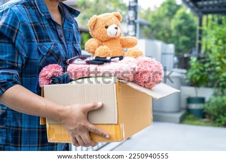 Holding clothing donation box with used clothes and doll at home to support help for poor people in the world. Royalty-Free Stock Photo #2250940555