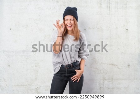 Beautiful young woman standing over grunge grey wall doing ok sign with fingers, excellent symbol