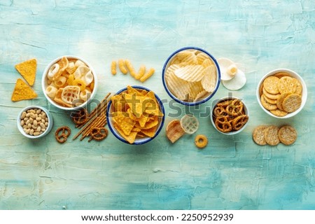 Salty snacks, overhead flat lay background with copy space. Party food on teal. Potato and tortilla chips, salt crackers and other appetizers