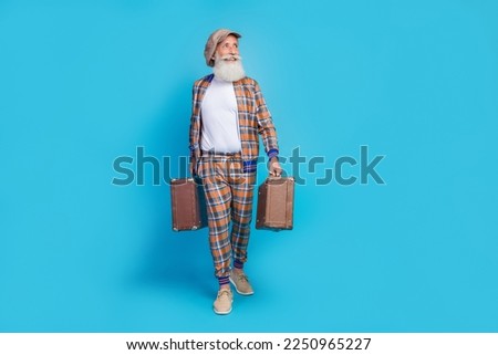 Full length photo of good mood man pensioner wear checkered costume looking empty space holding baggage isolated blue color background