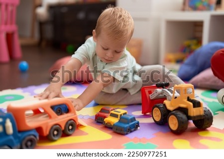 Adorable toddler playing with car toy sitting on floor at kindergarten