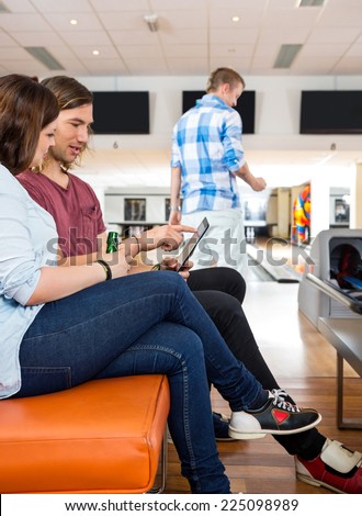 Side view of young man and woman using digital tablet on couch in bowling club
