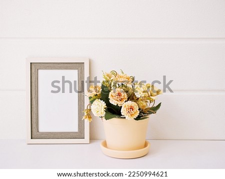 Artificial rose flowers in pot and empty photo frame on table with white wooden wall background ,Copy space for text ,Mother's day , ,Decoration home ,Copy space festive card ,Wedding concept