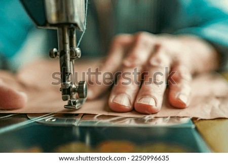 Senior woman in spectacles use sewing machine. wrinkled hands of the old seamstress.elderly woman . Old sewing machine Classic retro style manual sewing machine ready for sewing work.  Royalty-Free Stock Photo #2250996635