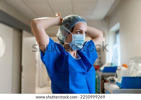 Nurse standing distracted while putting on her face mask in a hospital