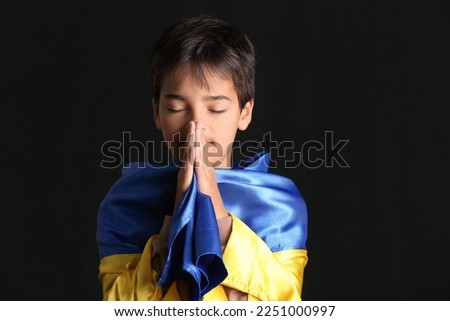 Little boy with flag of Ukraine praying on black background