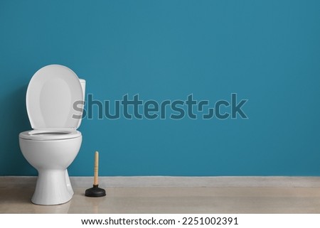 Ceramic toilet bowl and plunger near blue wall Royalty-Free Stock Photo #2251002391