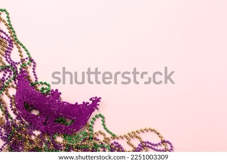 Mardi Gras beads and carnival mask on purple background. Mardi Gras holiday banner design. Flat lay, top view, overhead.