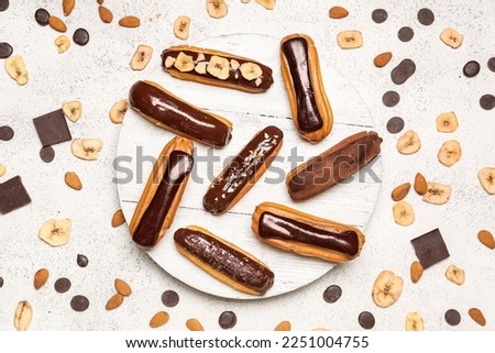 Wooden board with tasty chocolate eclairs, almond and banana chips on light background Royalty-Free Stock Photo #2251004755