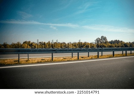 A beautiful shot of a highway guardrail on the side of a road with trees in the background Royalty-Free Stock Photo #2251014791