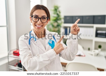 Young brunette doctor woman wearing stethoscope at the clinic smiling and looking at the camera pointing with two hands and fingers to the side. 