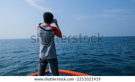 Tourist man taking photo with camera isolated on big ocean background, view from behind. Man standing on a boat while taking photos.