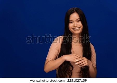 Brunette asian woman in t-shirt looking at camera isolated on blue