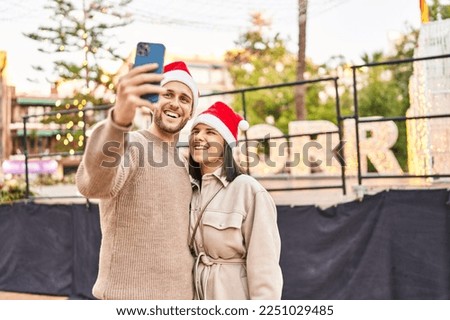 Man and woman couple wearing christmas hat make selfie by the smartphone at park
