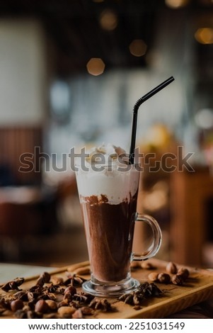 A close-up hot chocolate in a tall glass with whipped cream on a wooden board in a cafe
