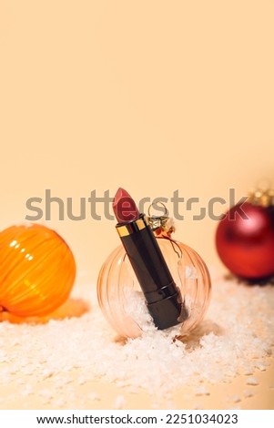 Composition with lipstick, broken Christmas ball and snow on color background