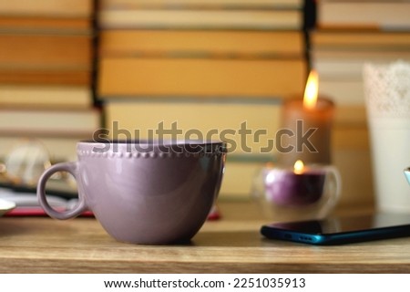 Notebook, pen, tablet, reading glasses, books, phone, candle, bowl of biscuits and cup of tea on the table. Selective focus.