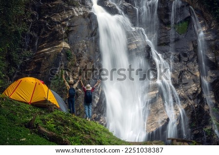 woman traveller walk togather Tent and camping with Mae Tia waterfall and mountain background at inthanon national park in Chiang mai, Thailand, un seen travel point for camping and relax in holiday