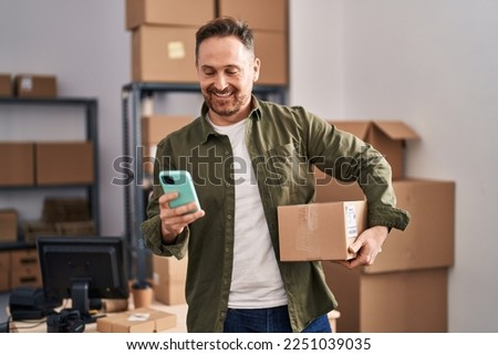 Young caucasian man ecommerce business worker using smartphone holding package at office Royalty-Free Stock Photo #2251039035