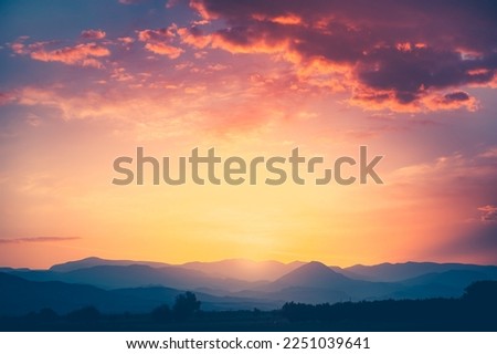 Spectacular sunrise over mountain range under mist in the morning light. Colorful clouds in orange sky. Amazing nature scenery background. Tourism and travel concept image. Copy space.