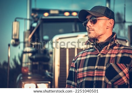 Proud Semi Truck Driver Portrait in Front of the Vehicle. Caucasian Trucker in His 40s Wearing Baseball Hat. Royalty-Free Stock Photo #2251040501