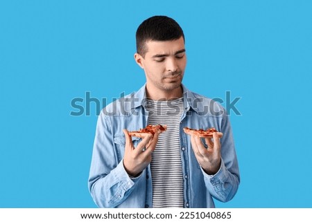Handsome young man with slices of fresh pizza on blue background