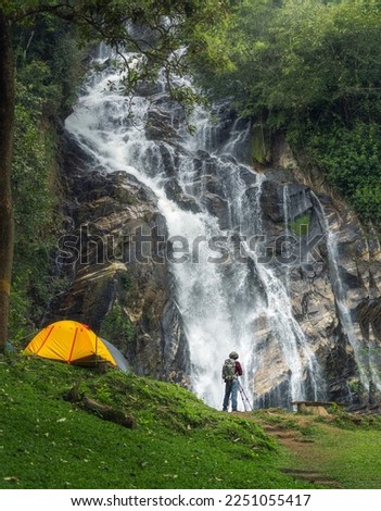 A man traveller walk togather Tent and camping with Mae Tia waterfall and mountain background at inthanon national park in Chiang mai, Thailand, un seen travel point for camping and relax in holiday