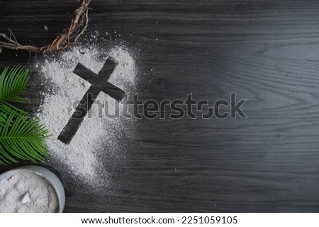 Border of cross of ashes, crown of thorns, palm leaves and bowl of ashes on a dark wood background with copy space Royalty-Free Stock Photo #2251059105