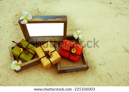 gift box and vintage style empty photo frame  lying on a sea sand decorated with flower background. Space for your text. vintage color tone