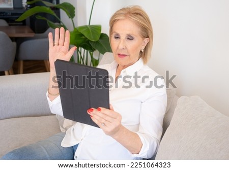 Smiling mature old woman holding using digital tablet relaxing sit on sofa reading e book in reader app, happy middle aged senior grandma browsing internet shopping online on pad computer at home
