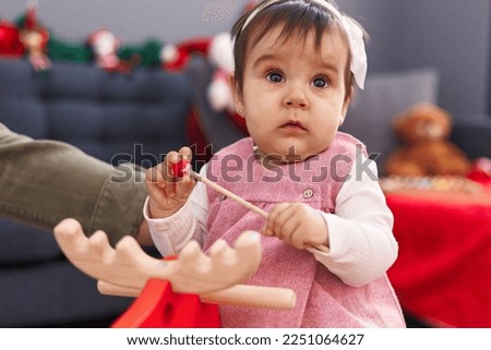 Adorable hispanic baby playing with reindeer rocking by christmas decoration at home