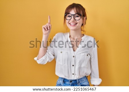 Young beautiful woman wearing casual shirt over yellow background pointing finger up with successful idea. exited and happy. number one.  Royalty-Free Stock Photo #2251065467