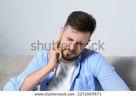 Young man suffering from ear pain at home Royalty-Free Stock Photo #2251069871