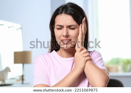 Young woman suffering from ear pain indoors Royalty-Free Stock Photo #2251069875
