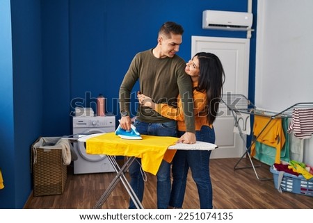 Man and woman couple hugging each other ironing clothes at laundry room