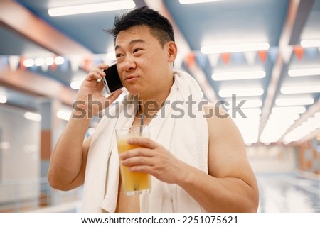 Asian man standing in indoors swimming pool and using a phone