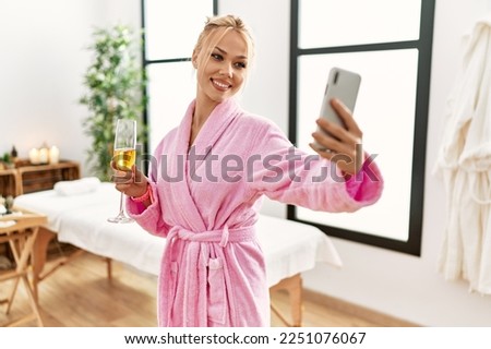 Young caucasian woman wearing bathrobe drinking champagne make selfie by smartphone at beauty salon
