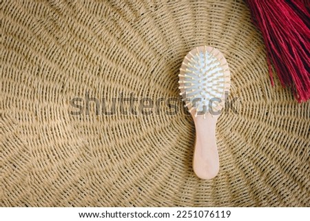 Small round wooden natural hair comb against the background of a wicker basket. Hair care. Simple minimalistic light photo. Empty space for text, design. Isolated organic eco cosmetic product.