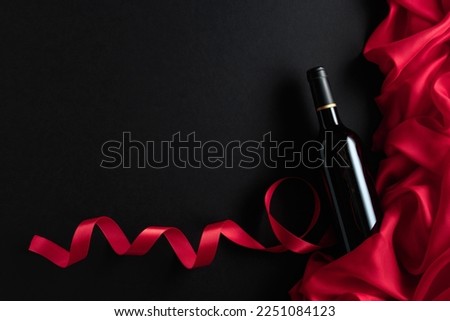 Bottle of red wine with red satin on a black background. Top view.