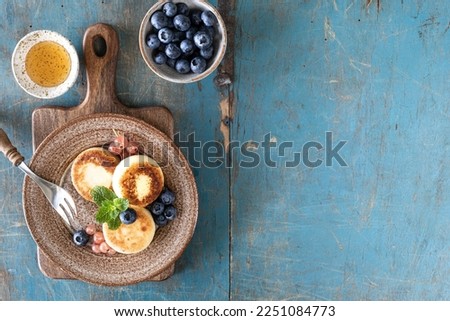 Cottage cheese pancakes, cheesecakes, ricotta fritters with fresh blueberries, currants and peaches on a plate. Healthy and delicious breakfast for the holiday. Blue wooden background. Top view