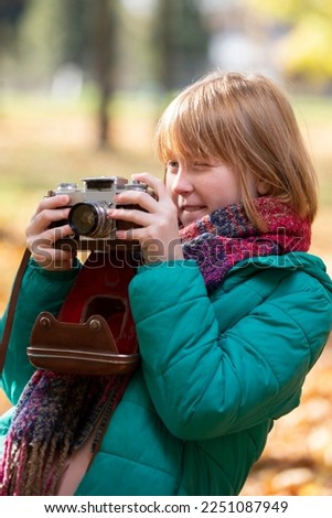 Little red-haired girl with a retro camera in the autumn park. Child photographer.