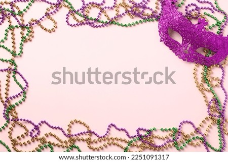 Frame of Mardi Gras beads and carnival mask on purple background. Mardi Gras holiday banner design. Flat lay, top view, overhead.