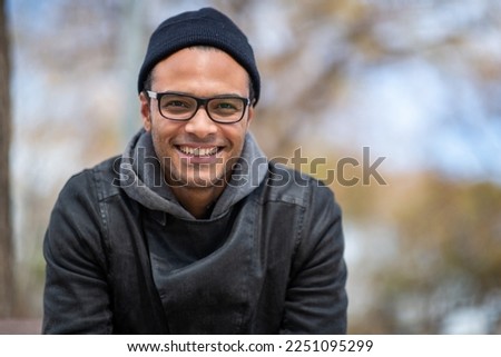 Close up portrait of handsome young african man in warm jacket and knitted hat looking at camera and smiling outside in the city Royalty-Free Stock Photo #2251095299