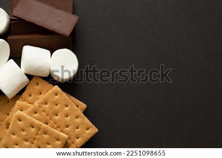 S'mores ingredients, graham crackers, marshmallows, chocolate bars with blank space to the right