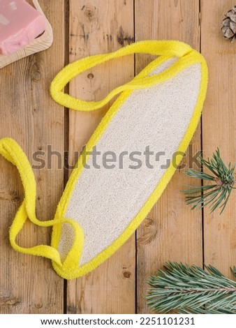 Washcloth for shower with yellow handles made of natural loofah on wooden background. Eco-friendly washcloth. Top view